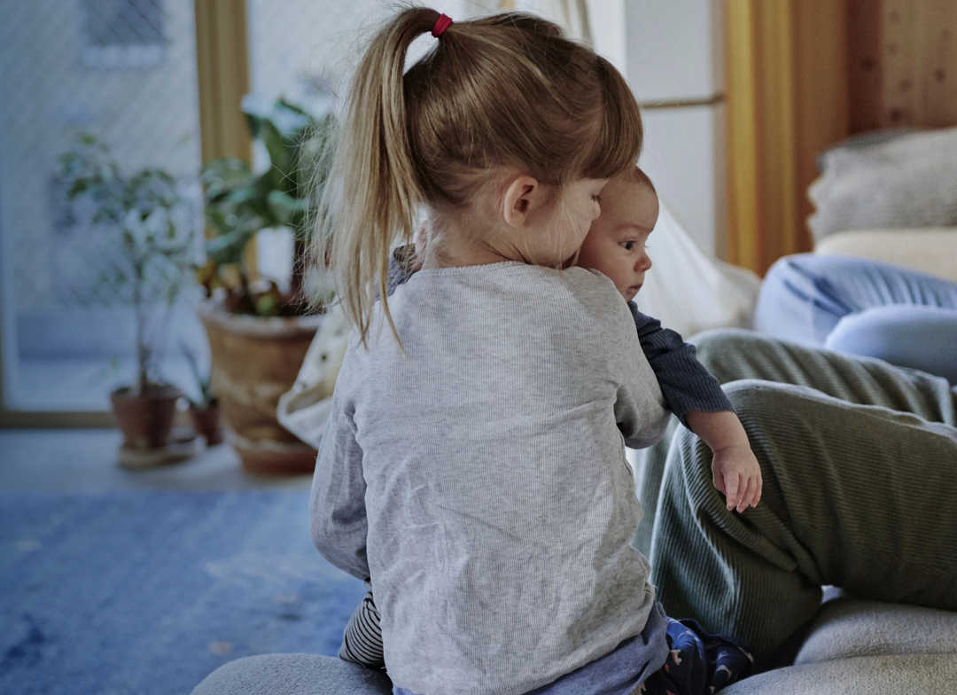 Ein Mädchen hält einen Säugling im Arm.